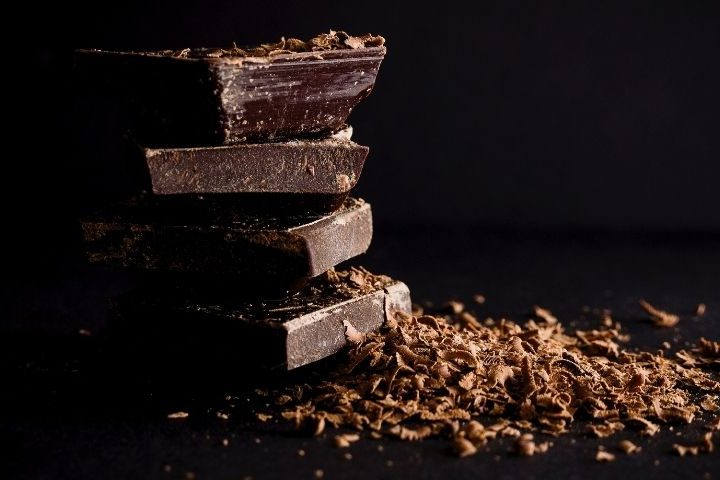 pile of dark chocolate squares on black background