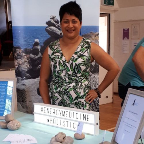 Neela standing in a green/white jumpsuit at her stand at wellbeing event