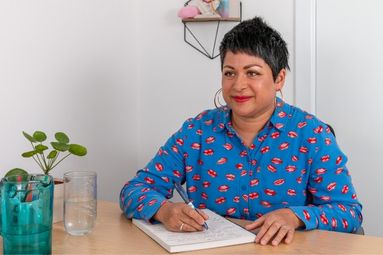Neela sitting at desk with writing pad on table and pen in hand