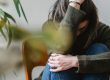 lady in jeans and jumper sat with knees up on wooden chair with arm around knees and hand on head