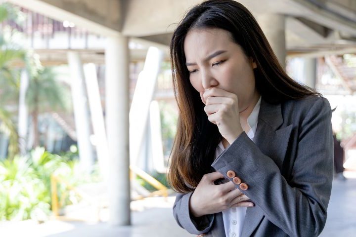 lady in grey suit holding chest and coughing