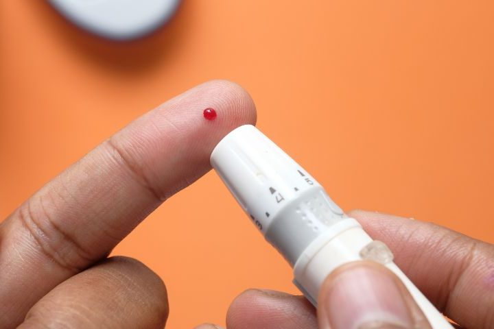 finger pricker just used to produce droplet of blood on opposite finger with orange background