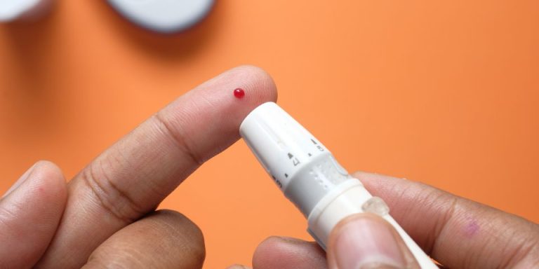 finger pricker just used to produce droplet of blood on opposite finger with orange background