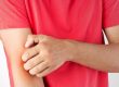 man in red tshirt scratching his inner elbow with opposite hand