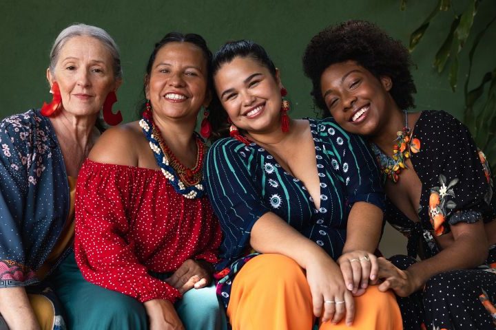 4 women all sat in a row on a sofa wearing colourful clothing