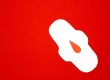 red background with a white sanitary pad and fake red droplet upon the pad
