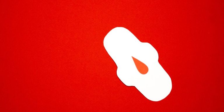 red background with a white sanitary pad and fake red droplet upon the pad