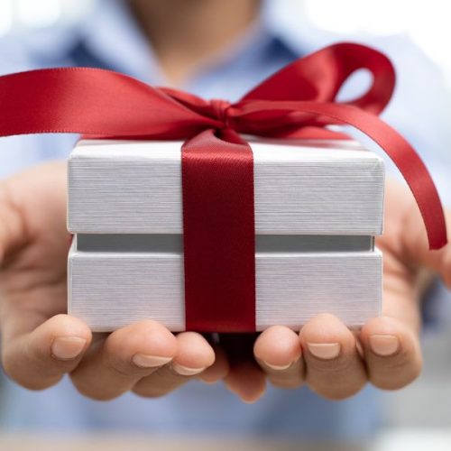 white gift box with red ribbon around it being held in 2 open outstretched hands