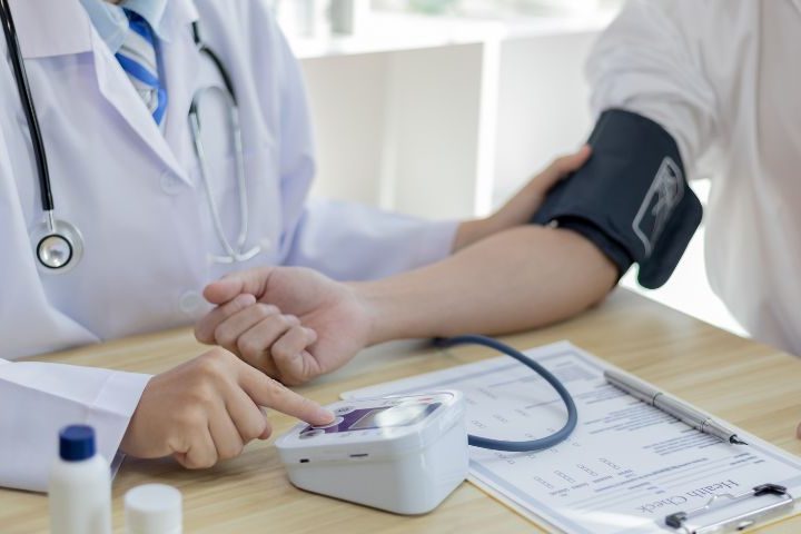 white coated doctor taking blood pressure of patient at table with electronic machine