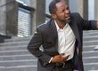man in business suit clutching his stomach in pain at bottom of external stairs