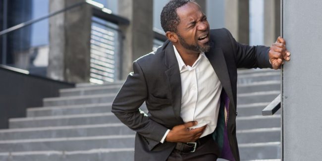 man in business suit clutching his stomach in pain at bottom of external stairs