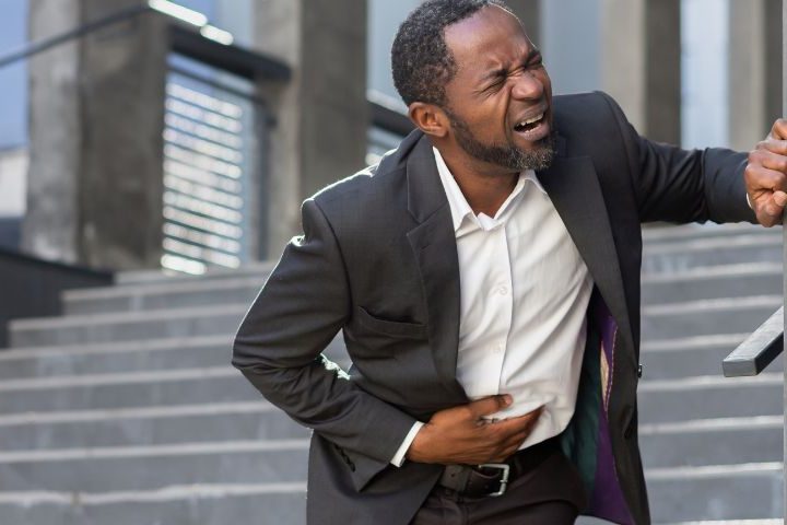 man in business suit clutching his stomach in pain at bottom of external stairs