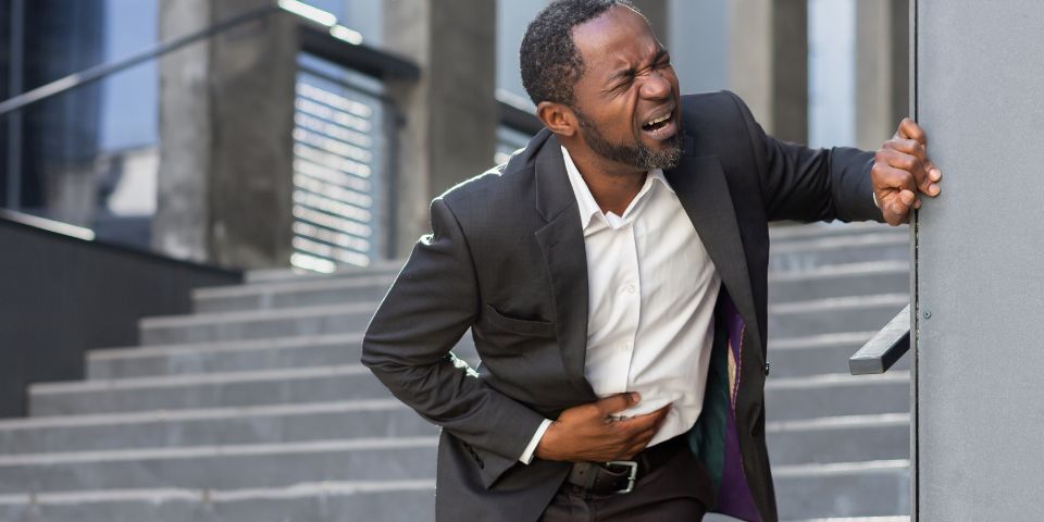 10yrs stomach pain man in business suit clutching his stomach in pain at bottom of external stairs