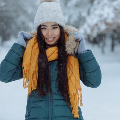 asian lady in snowy landscape wearing a warm coat, scarf and hat